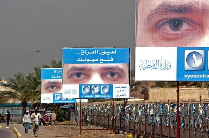 Iraqis walk under billboards showing posters urging people to report terrorist acts in Baghdad in 2006. The poster shows eyes of a man and a slogan that reads: &quot;For the sake of Iraq, open your eyes.&quot;Photo by Sabah Arar\/AFP\/Getty Images